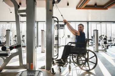 Tekerlekli sandalyedeki kullanıcı, son çekiş makinesinde egzersiz yaparak, kapsayıcı fitness ve rehabilitasyon gücünü gösterir.