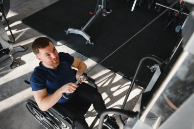 Tekerlekli sandalyedeki bir adam spor salonunda güçlü bir antrenman yapıyor, rehabilitasyon ve fitness yoluyla güç gösterisi yapıyor.
