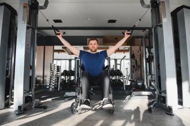 Engelli bir adam spor salonunda tekerlekli sandalyede ağırlıkla egzersiz yapıyor. Güç ve kararlılık gösteriyor.