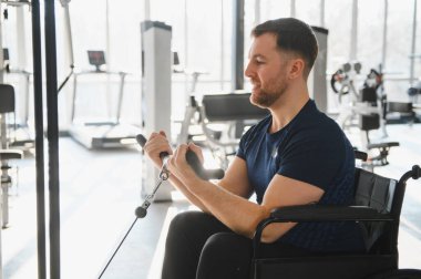 Tekerlekli sandalyedeki engelli adam, kollarını çalıştırıyor. Parlak bir rehabilitasyon salonunda ağırlık kullanıyor.