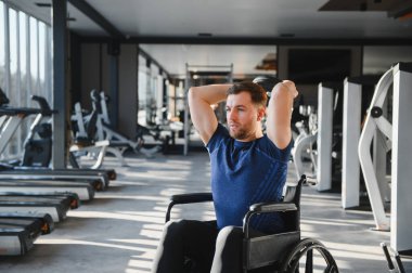 Tekerlekli sandalyedeki erkek sporcu ağırlık kaldırıyor, spor salonunda egzersiz yapıyor, rehabilitasyon sırasında direnç ve güç gösteriyor.