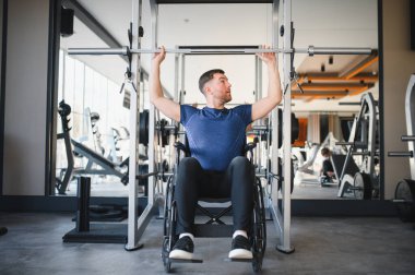 Tekerlekli sandalye kullanan odaklanmış erkek sporcu, modern bir spor salonunda ağırlık kaldırıyor, dayanıklılık, zindelik ve rehabilitasyona olan bağlılığını gösteriyor.