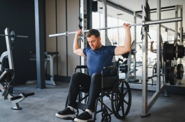 Tekerlekli sandalyedeki erkek sporcu spor salonundaki rehabilitasyon egzersizleri sırasında ağırlık kaldırıyor, dayanıklılık ve dayanıklılık gösteriyor