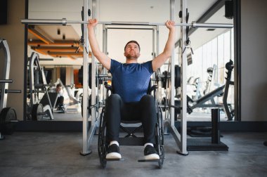 Tekerlekli sandalyedeki erkek sporcu ağırlık kaldırıyor, dayanıklılık, dayanıklılık ve spor salonundaki rehabilitasyona olan bağlılığını gösteriyor.