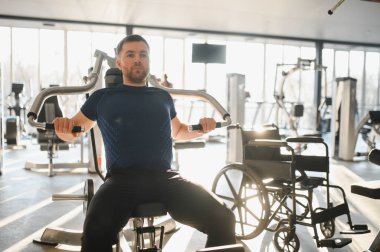 Parlak bir spor salonunda rehabilitasyon sırasında göğüs pres makinesi kullanan engelli biri.