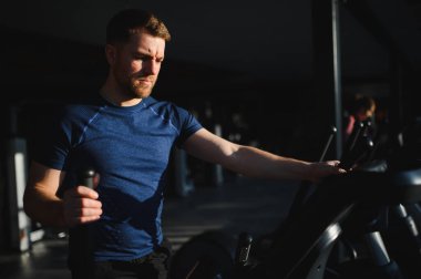 Fiziksel engelli bir adam rehabilitasyon salonunda adaptif ekipman üzerinde çalışıyor. Kararlı ifade iyileşme ve güç kazanma üzerine odaklandığını gösteriyor