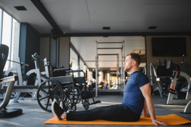 Özürlü erkek sporcu spor paspasının üzerinde esneme egzersizleri yapıyor, dayanıklılık ve spor yapmaya bağlılığını gösteriyor.