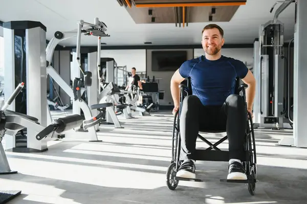 Tekerlekli sandalyedeki adam, parlak bir spor salonunda egzersiz yapıyor, engelliler için kapsayıcılık ve aktif yaşam tarzını destekliyor.