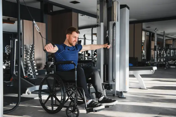 Adam spor salonunda rehabilitasyon egzersizlerine katılıyor, gücü arttırmak ve iyileşmeyi hızlandırmak için kablo makinesini kullanıyor.