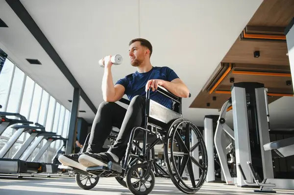 Tekerlekli sandalyedeki kararlı adam halteri kaldırıyor, egzersiz yapıyor ve spor salonunda rehabilitasyona gidiyor.