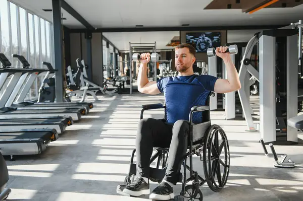 Özürlü bir adam, tekerlekli sandalyeli bir sporcu halterleri kaldırıyor, egzersiz yapıyor ve modern bir rehabilitasyon salonunda güç topluyor.