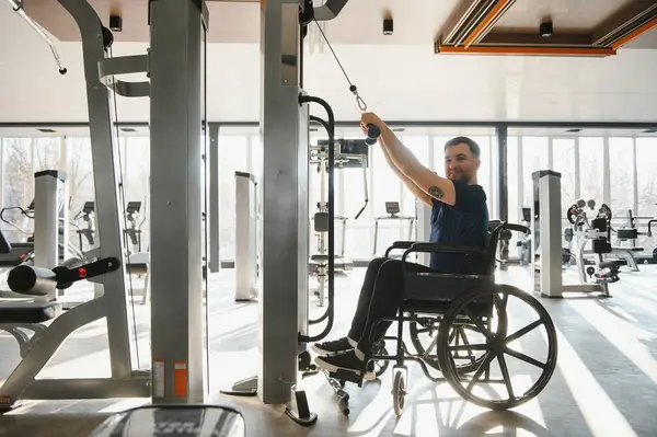 Tekerlekli sandalyedeki kullanıcı, son çekiş makinesinde egzersiz yaparak, kapsayıcı fitness ve rehabilitasyon gücünü gösterir.