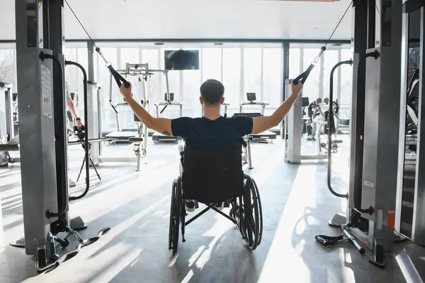 Bir spor salonunda kablo ağırlıklarıyla rehabilitasyon egzersizleri yapan hasta fiziksel zorlukların üstesinden gelmede kararlılık ve güç gösteriyor.