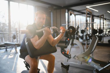 Spor salonunda ağırlık kullanan kararlı bir adam egzersiz yaparak rehabilitasyona ve iyileşmeye odaklanıyor.