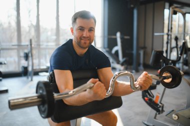 Odaklanmış sporcu, modern bir fitness merkezinde bir ez çubuğuyla biseps kıvrımları, rehabilitasyon ya da güç eğitimi görüyor