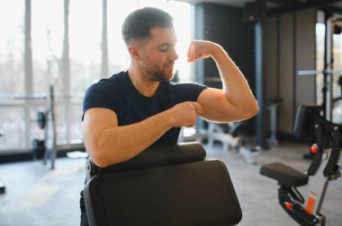 Tekerlekli sandalyedeki bir adam spor salonunda kaslarını kasıyor, fitness ortamında gücünü ve rehabilitasyonunu ön plana çıkarıyor.