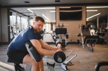 Azimli bir adam ağırlık kaldırıyor, kaslarını çalıştırıyor modern bir rehabilitasyon salonunda vaiz kürsüsü kullanıyor, iyileşme ve dayanıklılık eğitimine odaklanıyor.