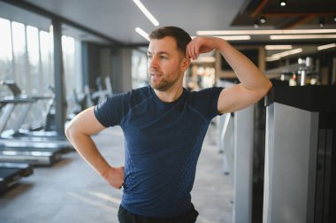Spor salonunda teçhizata bel bağlayan, rehabilitasyona ve forma odaklanan bir adam. Fiziksel zorlukların üstesinden gelmek için güç ve kararlılığı simgeler.