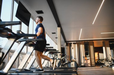 Koşu bandında koşan kararlı erkek sporcu, geniş pencereli modern spor salonunda rehabilitasyon için egzersiz yapıyor.