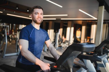 Modern spor salonunda eliptik çapraz antrenör üzerinde egzersiz yapan sakallı sporcu, spor rehabilitasyonu görüyor.