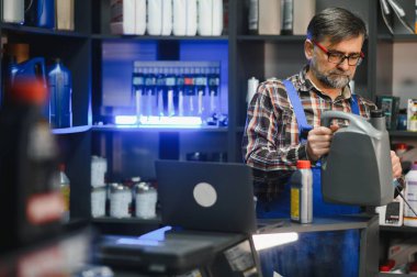 Kıdemli satıcı bir oto yedek parça mağazasında büyük bir şişe motor yağı tutuyor, etiketi kontrol ediyor.