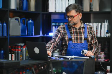 Üniformalı kıdemli satıcı oto yedek parça mağazasında çalışıyor. Dizüstü bilgisayar ve barkod tarayıcı kullanarak mal bulunup bulunmadığını kontrol ediyor.