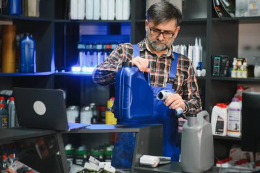 Satış elemanı, çeşitli otomotiv ürünlerinin raflarıyla çevrili bir oto yedek parça mağazasında çalışırken, motor yağını barkod tarayıcısıyla tarıyor.