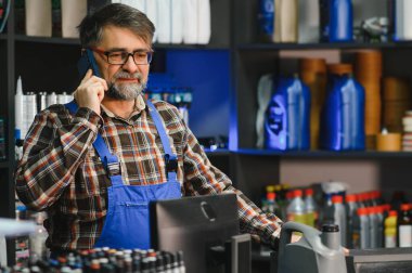 Yedek parça mağazasında çalışan mavi tulumlu kıdemli satıcı telefonla sipariş alıyor.