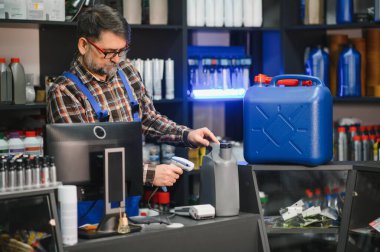 Satış elemanı, bir oto yedek parça mağazasının tezgahında motor yağını tarayarak müşterilerin işlemlerini kolaylaştırıyor.