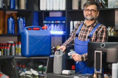 Satış elemanı bir oto yedek parça mağazasında motor yağını tarayıcı ile tarıyor, müşterilere ihtiyaçları konusunda yardımcı olurken envanteri yönetiyor.