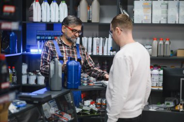 Bir oto yedek parça mağazasında müşteriye farklı motor yağı seçenekleri gösteren tamirci, araç bakımı için uzman tavsiyesi sunuyor