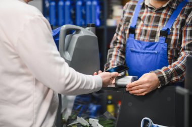 Müşteri, araba parçası almak için akıllı telefon kullanıyor. Satıcının da yardımıyla bir oto-gereç dükkanında.