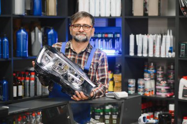 Bir oto yedek parça mağazasında müşteriye yeni bir araba farını sunan satıcı, ürünün özelliklerini ve faydalarını vurguluyor