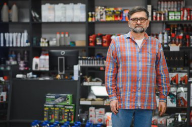 Kendine güvenen bir satıcı, çeşitli araba bakım ürünleriyle dolu raflarla çevrili bir oto yedek parça mağazasında duruyor ve müşterilere yardım etmeye hazır.