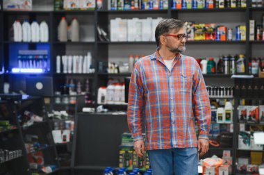 Oto yedek parça mağazasında yürüyen kıdemli satıcı motor yağı, araba bakım ürünleri ve aletlerle dolu rafları kontrol ediyor.