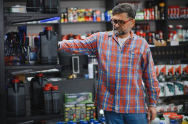 Kıdemli tamirci, motor yağını raftan seçiyor, oto yedek parça mağazasından araba bakım ürünleri alıyor.