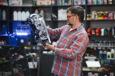 Bir oto yedek parça mağazasında yeni bir far gösteren kıdemli bir satıcı müşteriye satın almada yardım ediyor.