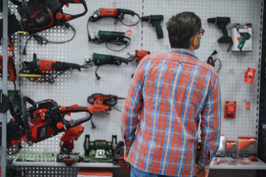 Müşteri hırdavatçıda duvara asılı elektrikli aletlere bakıyor, elektrikli testere ya da elektrikli tornavida seçiyor