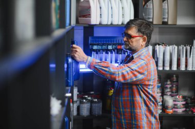 Kıdemli satıcı motor yağı şişesini raftan alıyor, oto yedek parça mağazasında çalışıyor, ürünleri ve envanteri kontrol ediyor.