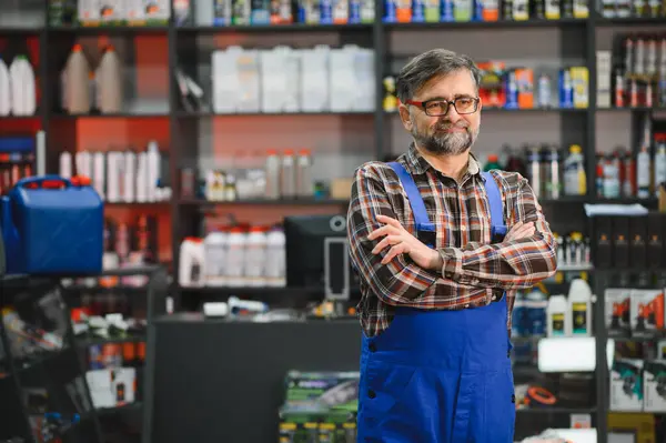 Kollarını kavuşturan bir satıcının portresi, iyi stoklanmış bir oto yedek parça mağazasında güvenle duruyor, müşterilere yardım etmeye hazır.