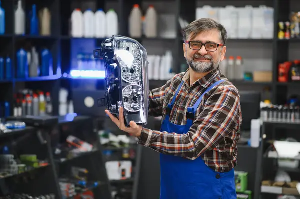 Kıdemli satıcı araba yedek parça dükkanında yeni bir araba farı gösteriyor, yedek ve araba bakım konsepti