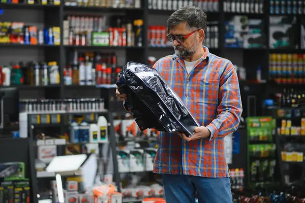 Satış elemanı otomobil yedek parça mağazasında bir araba farını inceliyor. Etrafı ürünlerle dolu.