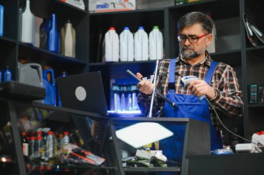 Kıdemli satıcı, oto parçalarını barkod tarayıcı ile tarıyor, oto yedek parça deposunda dizüstü bilgisayarla çalışıyor.