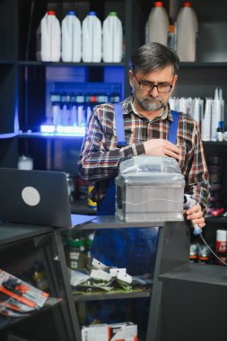 Satış elemanı otomobil yedek parça mağazasındaki araba aküsünde barkod tarayıcısı kullanıyor. Etrafı ürünlerle çevrili ve dizüstü bilgisayar kullanıyor.