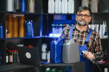 Satış elemanı motor yağı ve barkod tarayıcısı tutuyor, müşterilere yardımcı olurken aynı zamanda yedek parça mağazasında envanter yönetiyor.