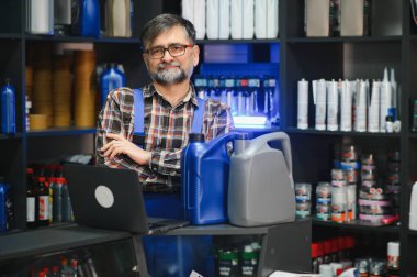 Dizüstü bilgisayarı tezgahta, oto yedek parça mağazasında, motor yağı şişelerinin yanında duran kıdemli satıcı.