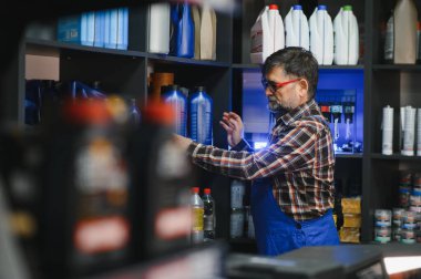 Kıdemli satıcı, motor yağı şişelerini bir rafa diziyor, oto yedek parça mağazasında çalışıyor, ürünlerin iyi organize edilmesini ve müşteriler tarafından erişilebilir olmasını sağlıyor.