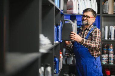 Satış elemanı oto yedek parça mağazasında büyük bir şişe motor yağı tutuyor, envanterleri kontrol ediyor ve müşterilere otomotiv ihtiyaçları konusunda yardımcı oluyor.