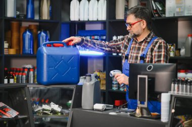 Otomobil parçaları satan adam barkod tarayıcı ile büyük mavi yağ bidonunu tarıyor, fiyatı kontrol ediyor ya da envantere ekliyor