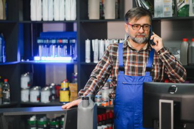 Mavi tulumlu satıcı bir müşteriyle telefon görüşmesi yapıyor. Otomobil parçaları ve hizmetleri konusunda uzman tavsiyesi veriyor.